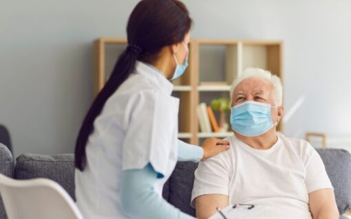 Nurse assisting elderly patient in long-term care facility, following infection control policy and procedures