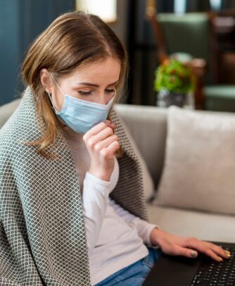 Woman wearing face mask coughing at home